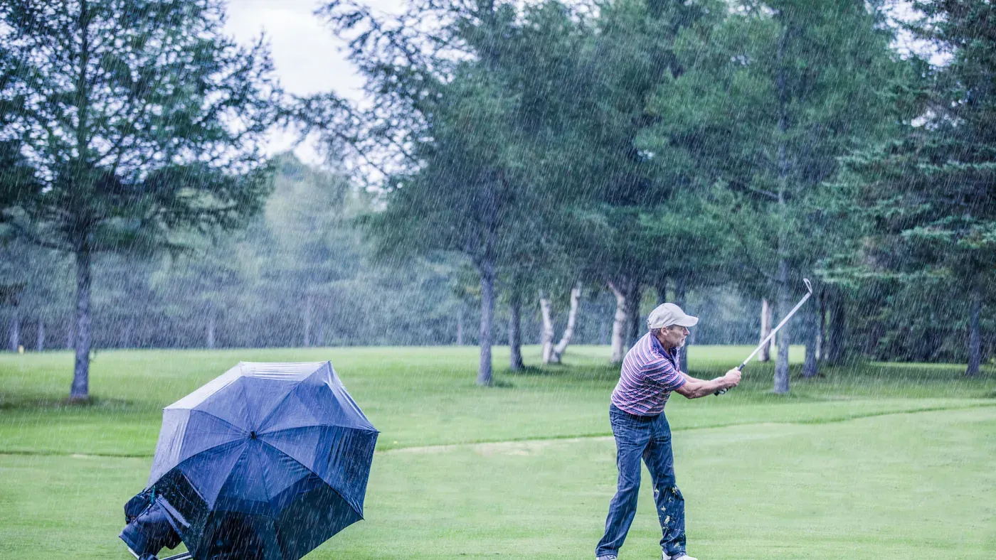 Golfare som slår ett slag på fairway under en regnig dag
