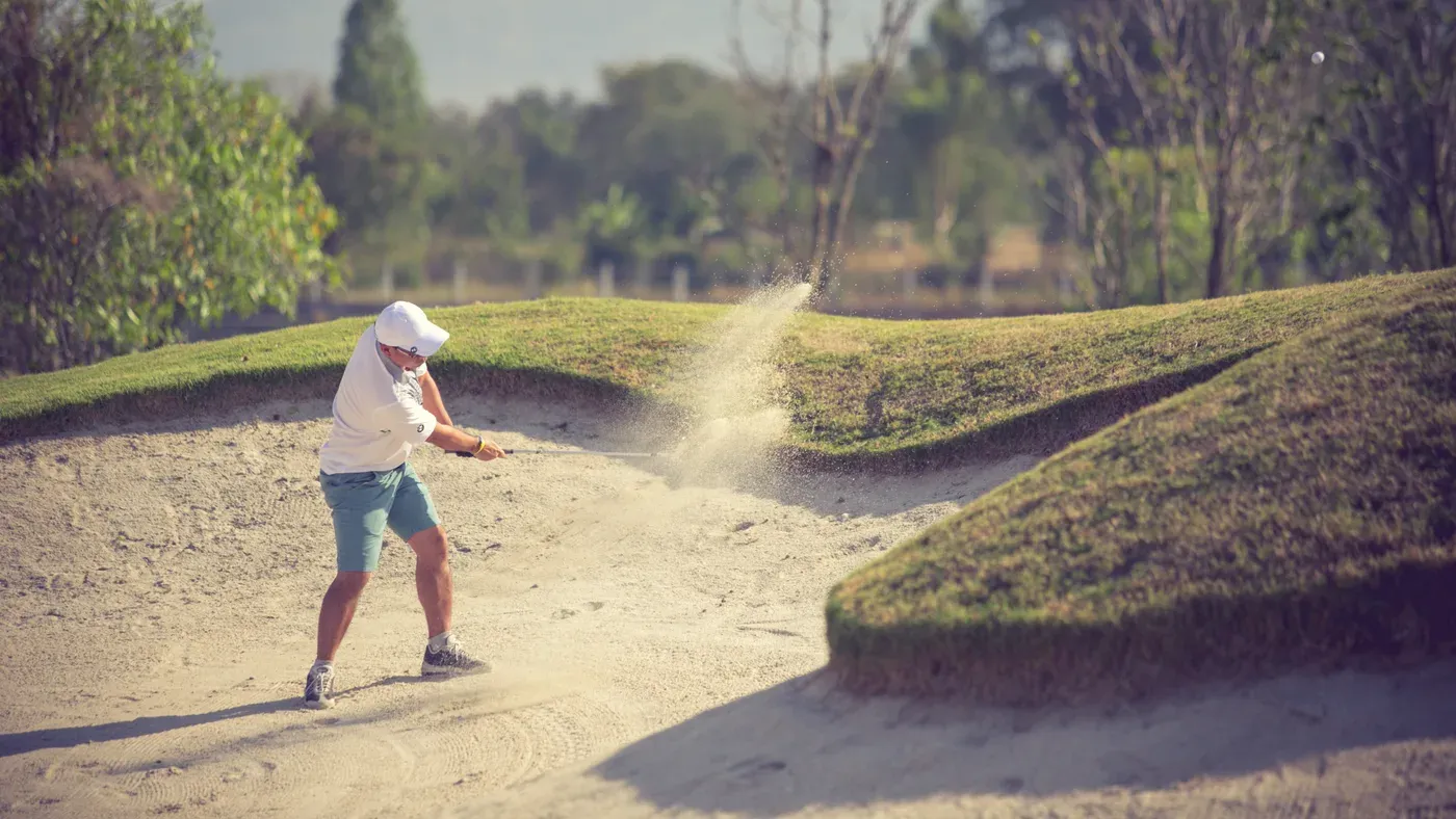 Golfare som slår ut ur en bunker med sanden yrande