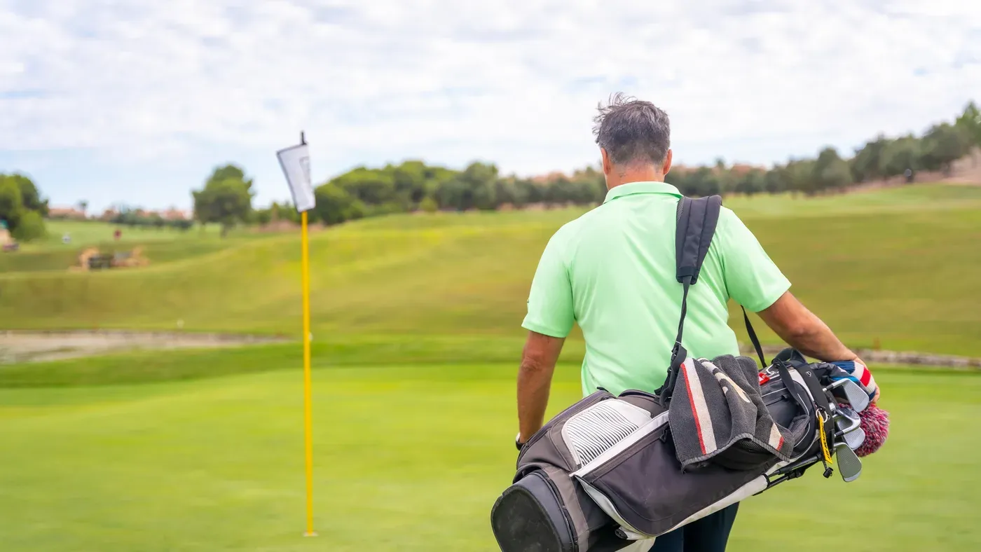 Golfare som bär sin golfbag på väg mot green