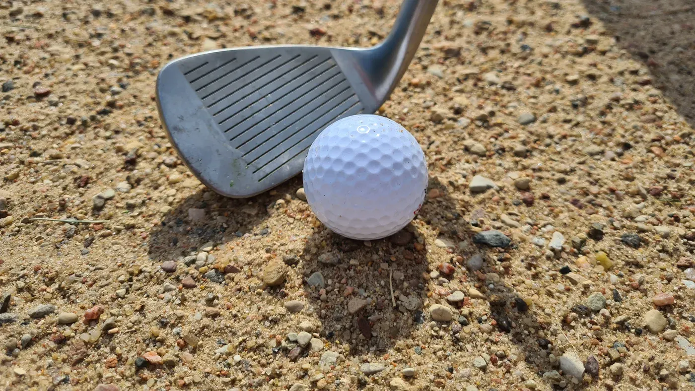 Järnklubba bakom golfboll i sanden i närbild