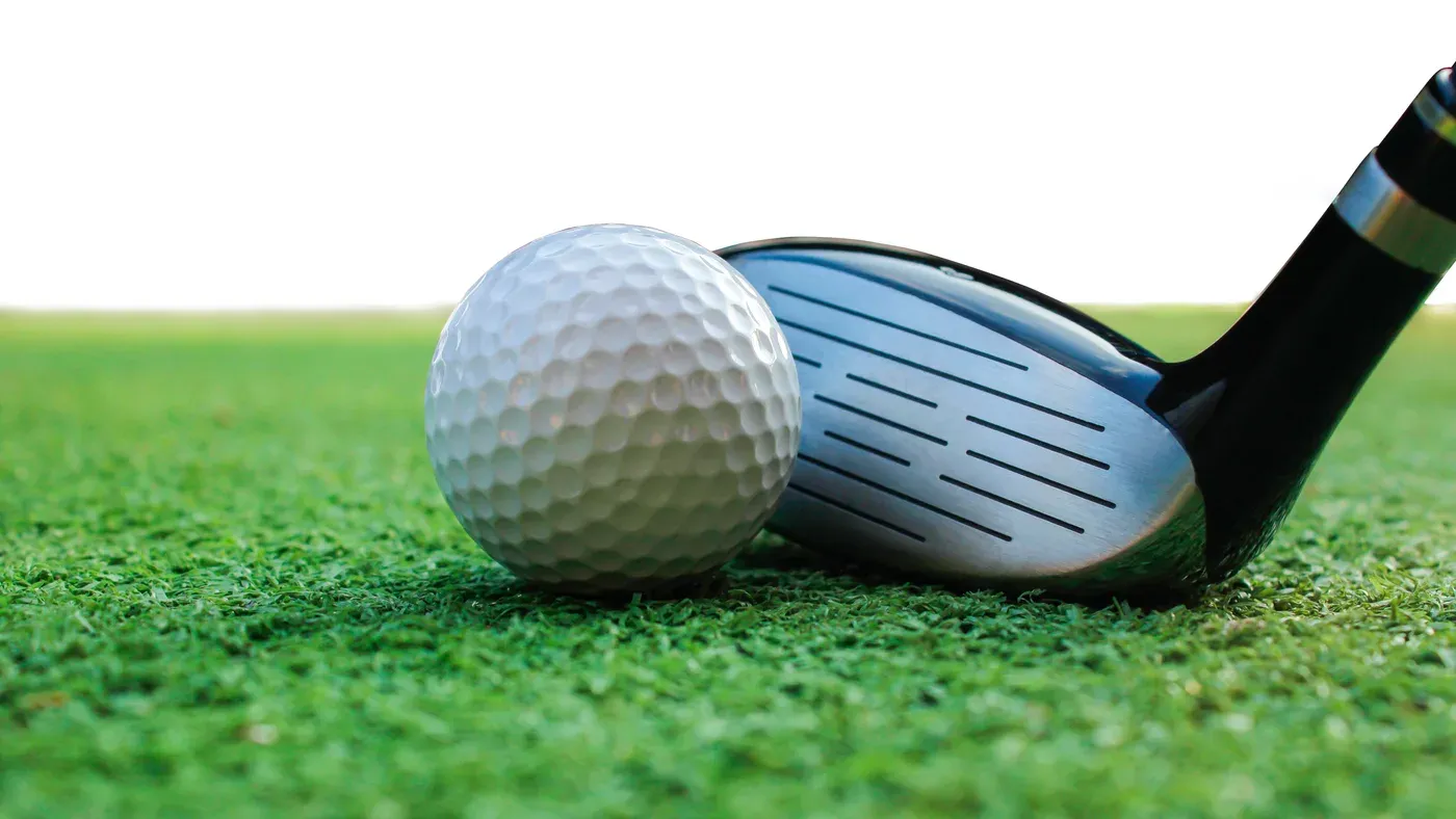 Klubbhuvud på fairwayträ bakom golfboll i närbild
