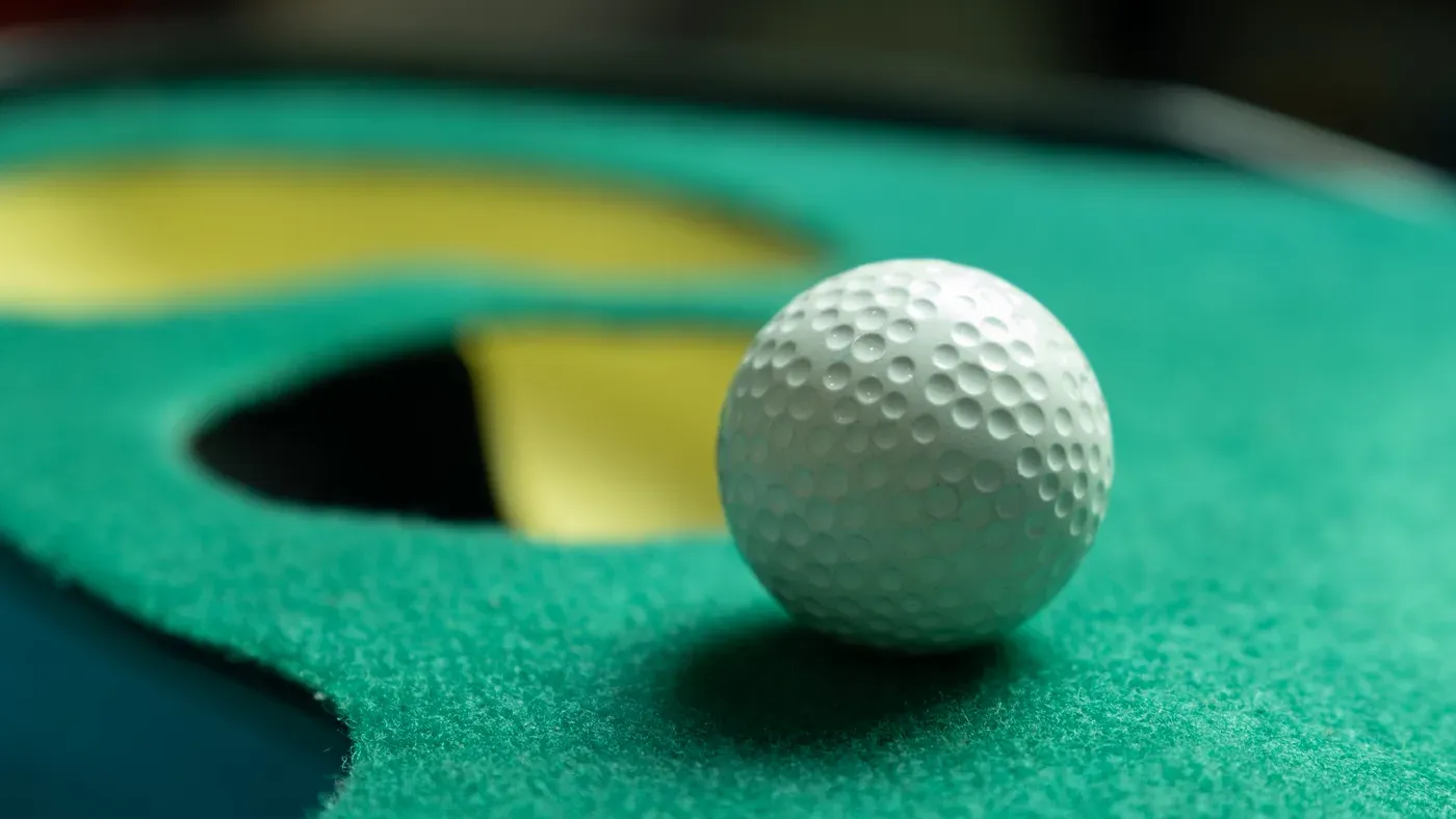 Golfboll stannar vid hålkanten på grön träningsmatta